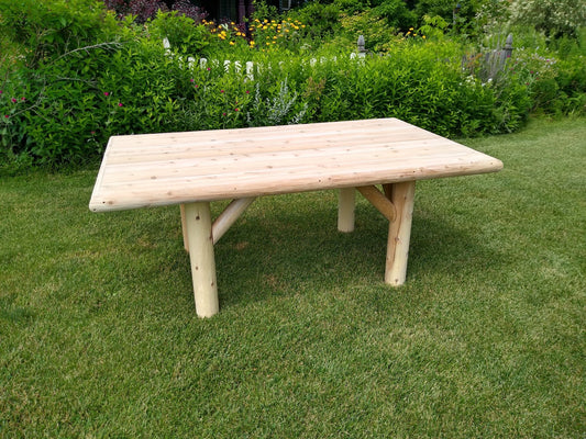 Rustic outdoor patio table made of natural wood, set on a green lawn with a lush garden in the background.